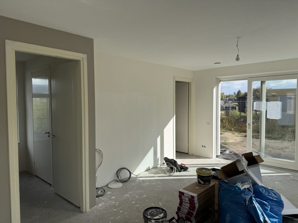 Open woonruimte in een net opgeleverd huis met een gesausde vliesmuur, openstaande binnendeuren en dozen laminaat