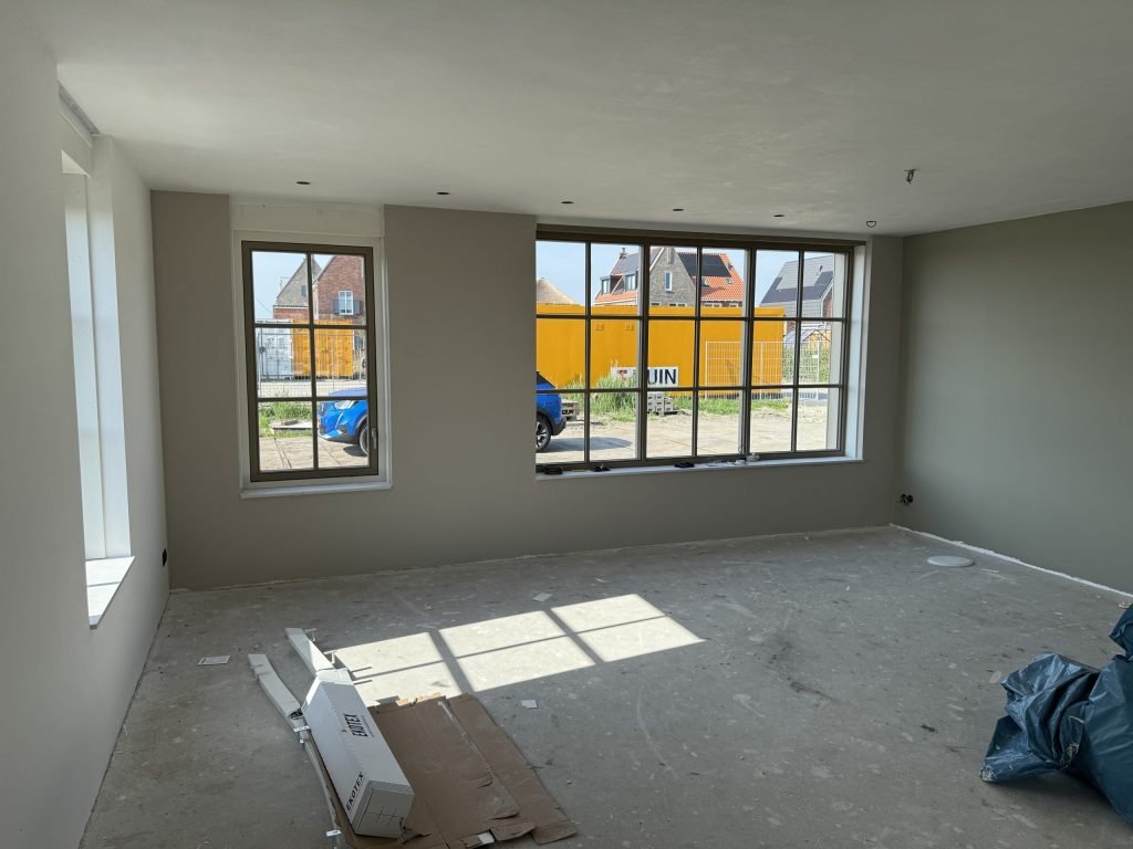 Lege woonkamer in een nieuwbouwwoning met strakke wanden in lichte kleuren en ramen met roedes naar de straat